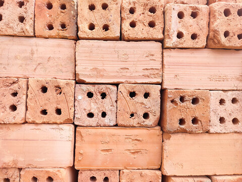 Close-up texture of stacked red clay bricks featuring four holes. Ideal background pattern showcasing raw masonry materials and construction craftsmanship.