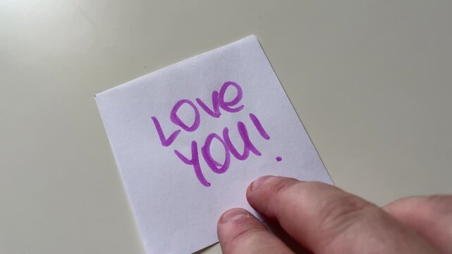 Hand Placing Sticky Note with Love You Message Close Up