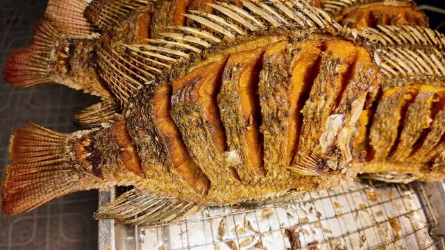 Extreme close-up of a whole crispy deep fried fish with golden crunchy skin displayed at a Thai street food market in Thailand. Authentic Asian seafood with detailed crispy texture ready to serve. 4K.