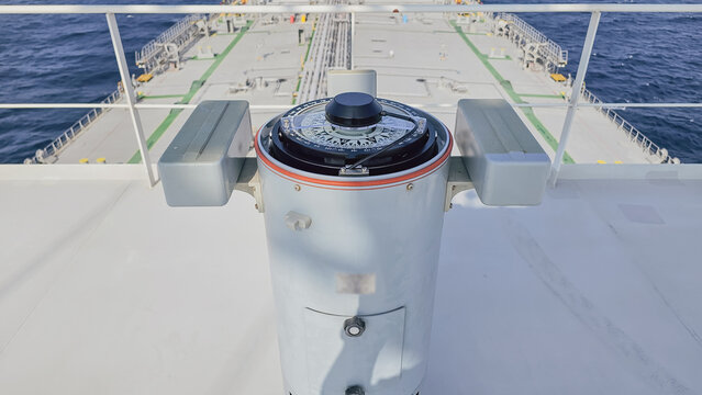 High angle view of gyro compass repeater on vessel navigation bridge wing facing ship deck and open sea water background during sunny maritime voyage day