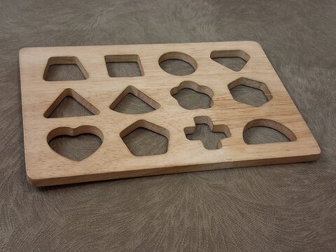 Wooden shape sorting puzzle board with multiple geometric cutouts placed on a textured fabric surface.