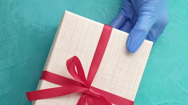 Gift delivery. Pandemic holidays. Hands in protective gloves bringing wrapped present boxes on teal blue textured background set of 4.
