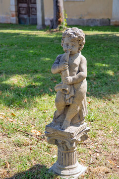 Stone cherub statue playing flute in Dajla monastery garden, Croatia.