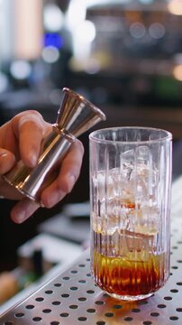 Vertical video. Mixologist work. Making cocktail. Bartender pouring sweet aroma color syrup from metal jigger to glass. Flavored refreshing drink.
