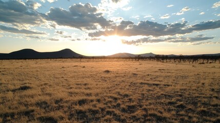 Fototapeta premium Peaceful summer evening sunset over a vast, dry plateau landscape with distant mountains and clouds