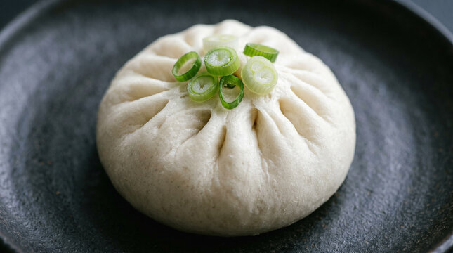 Steamed bao bun with scallions on dark plate.
