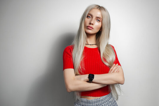 Young pretty blonde girl in red shirt with crossed hands isolated on grey background.