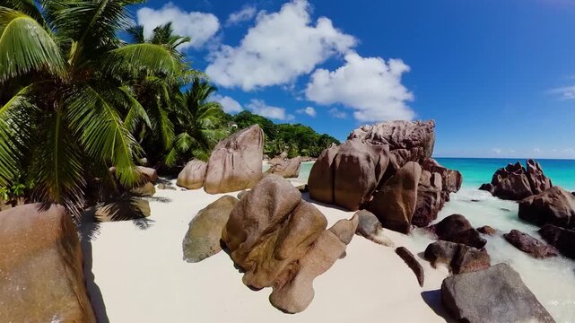 A tropical beach with soft white sand, smooth granite formations, and swaying palm trees. Anse Patates. Seychelles, La Digue.