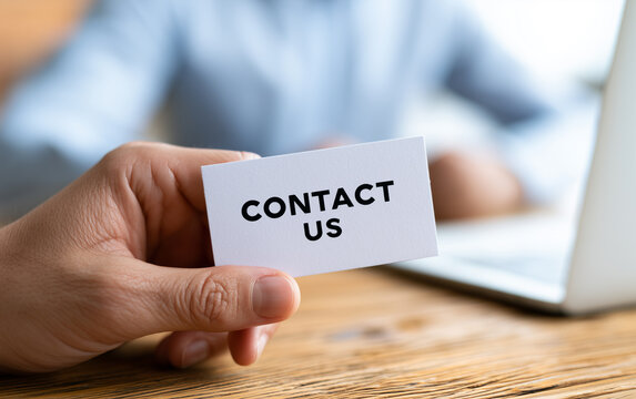 Hand offering a white paper sign with the text CONTACT US, inviting connection and communication