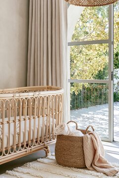 Boho nursery featuring natural rattan crib, woven jute basket, and warm sand cream walls illuminated by dappled afternoon light