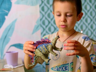 Close up of a little boy's hands playing with a plastic toy dinosaur. Early childhood imaginative play, storytelling, and indoor fun © light