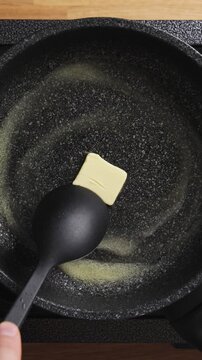 Butter melts quickly in hot frying pan, ready for cooking. Melted butter creates golden base for fluffy homemade pancakes. Butter and pancake combo makes classic breakfast recipe favorite.