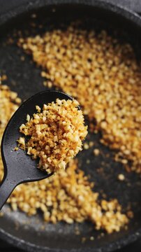 Spoon holds crunchy topping of fried nuts and panko, close up. Crunchy topping works great as crouton alternative on fresh salad. Nut and panko topping adds texture to healthy salad recipes.
