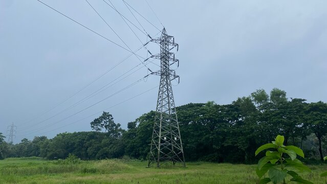 High voltage transmission tower pylon in green rural field landscape