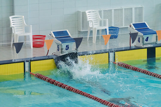 Swimmer diving into an indoor swimming pool during a competition. Splash at the start from a starting block with racing lanes, sports facility, and aquatic training environment