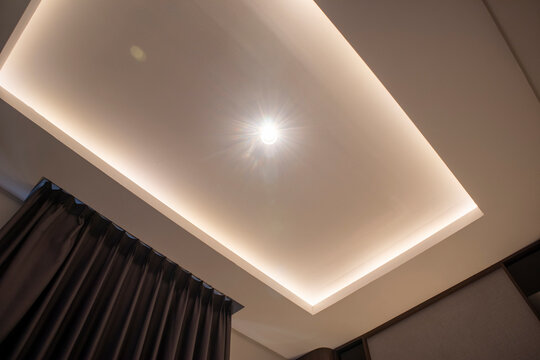 Modern false ceiling with recessed LED strip lighting, a central spotlight, and dark curtains