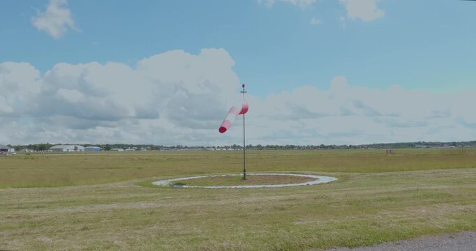 Red and white windsock on airfield under cloudy sky
