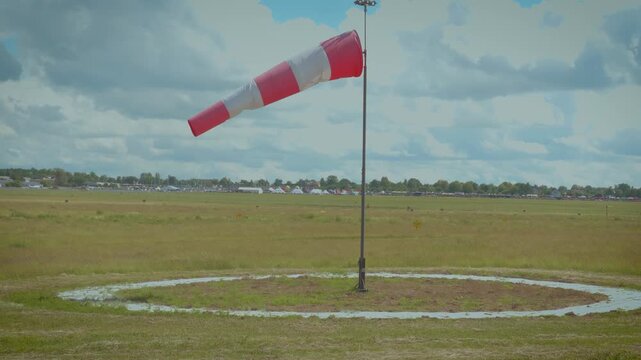 Windsock indicating wind direction on airfield runway under cloudy sky