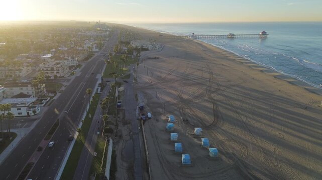 Aerial view reveals luxury coastal real estate along Pacific Coast Highway PCH in Huntington Beach, CA. Premium beachfront properties overlook expansive ocean views and piers in morning sunlight