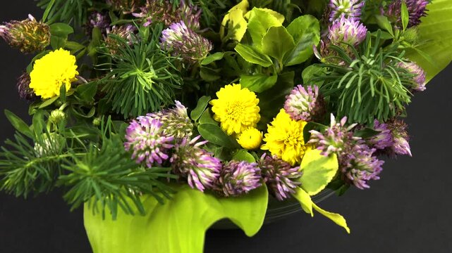 Flower arrangement of ornamental garden plants in a glass bowl, black background, top view