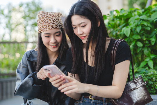 Two young asian woman gen z sisters using smartphone at outdoor park