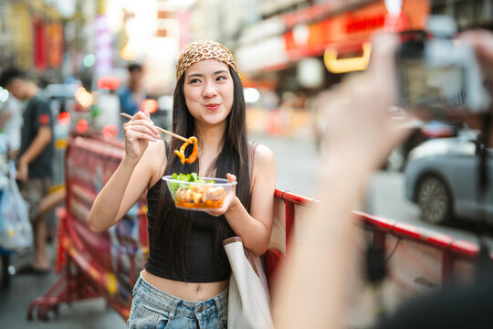 Two young asian woman gen z sisters eating spicy grilled squid enjoy Asia travel tasty street food