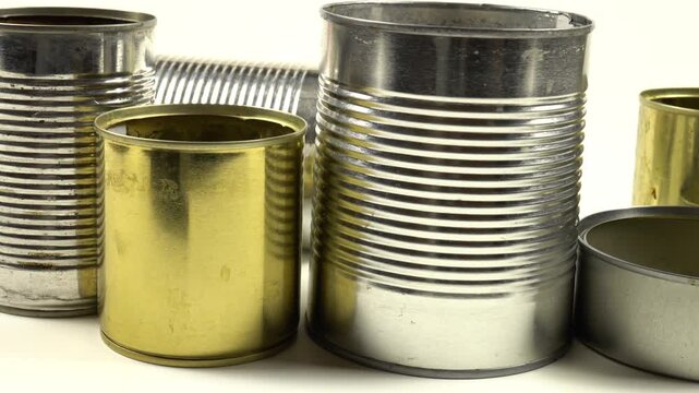 Different empty steel cans for storage of food are on a white table, side view