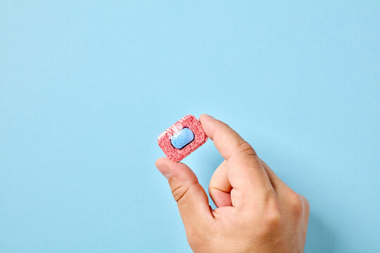 Hand holding single dishwasher detergent tablet on blue background