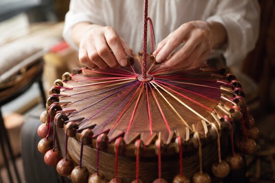 Hands braiding colorful silk cords on traditional round wooden stand