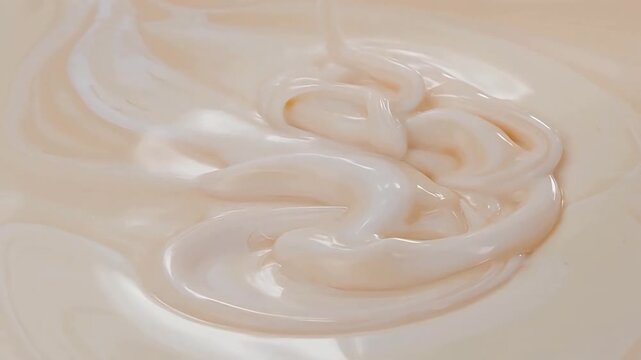 Close-up of creamy liquid being poured, forming swirling patterns on a smooth surface