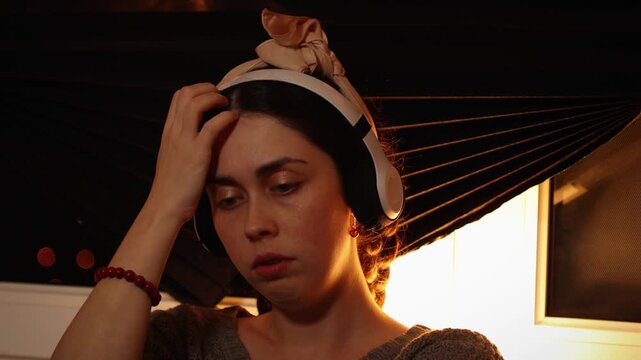Portrait of a young Caucasian woman wearing headphones, listening to music and staring blankly into the distance while nervously touching her face. Anxiety, neurotic behavior, psychological distress