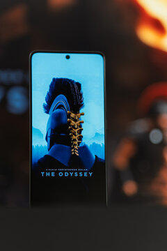 Screen displaying The Odyssey film poster by Christopher Nolan against blurred movie backdrop, cinema entertainment and mobile screen concept.