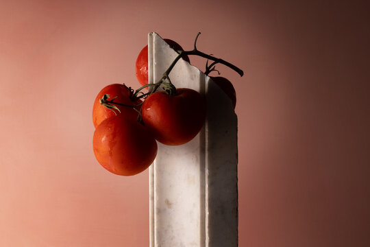 Grappolo di pomodori rossi su elemento in marmo bianco e fondo rosato, natura morta minimalista con spazio per il testo