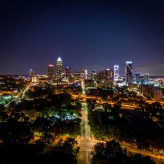 Fototapeta premium A nighttime aerial view of a cityscape with illuminated skyscrapers and streets surrounded by trees