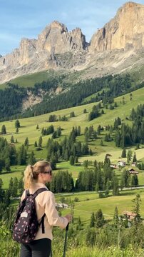 Woman hiking with trekking poles overlooking the majestic Catinaccio (Rosengarten) massif in the Dolomites, Italy. Scenic alpine landscape, outdoor adventure and slow living travel