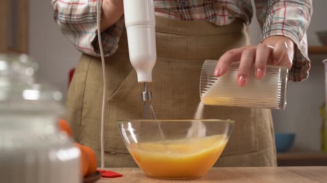 woman pastry chef in apron whips an egg yolk in a bowl with mixer.