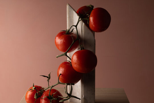 Grappolo di pomodori rossi su elemento in marmo bianco e fondo rosato, natura morta minimalista con spazio per il testo