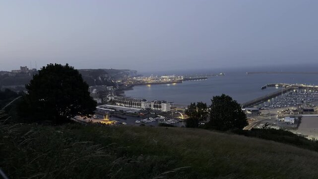 Illuminated port town from grassy hill panning