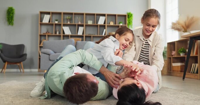 Family parents children daughters tickling playing laughter bonding. Parents and kids laugh on the carpet at home, relaxing, cuddling, and making memories. Concept of joyful family bonding.