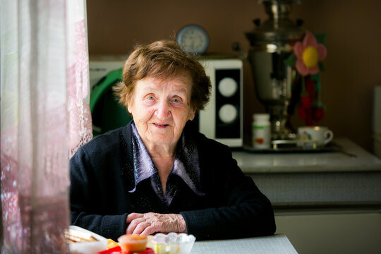 Smiling elderly woman sitting at a kitchen table in a cozy home illuminated by natural window light creating a warm and authentic lifestyle portrait