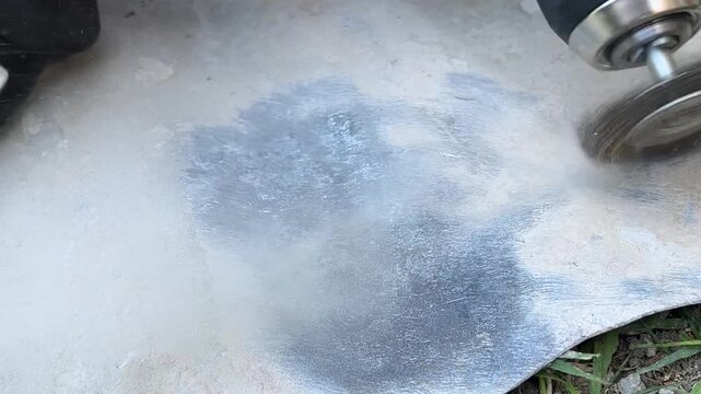 Close-up view of a worker's hand using a power drill with a spinning circular wire brush to remove old paint and rust from a metal surface, preparing it for restoration
