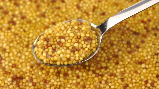 French Dijon mustard in a metal spoon, top view on mustard grains background. Gastronomy concept, organic food. Sauce. Slow rotation in a circle.	
