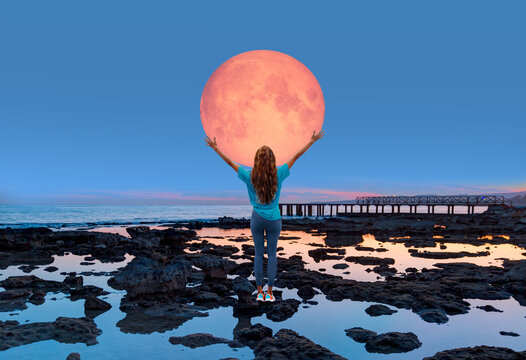 A beautiful woman is trying to catch the super full moon in the sea at sunset "Elements of this image furnished by NASA"