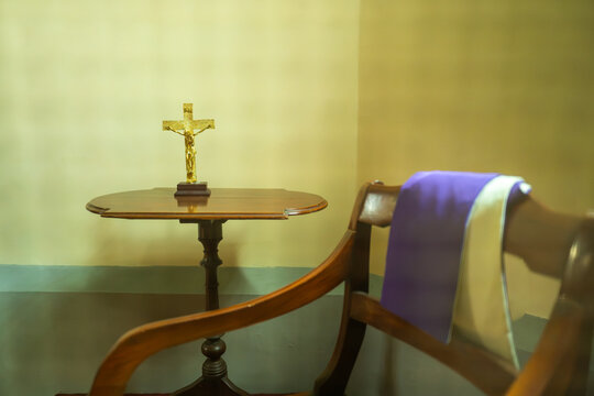 Golden Crucifix on Wooden Table Next to Confessional Chair with Priest Stole