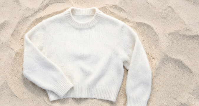 Immagine con capo di abbigliamento in morbida lana di color bianco adagiato su uno sfondo di fine sabbia di una spiaggia