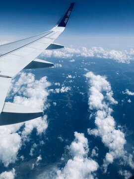 Airplane flight. View of airplane white wing flying in blue sky over clouds.