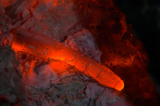 Glowing red hot wood embers burning with gray ash macro shot for campfire heat and energy concept