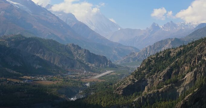 Annapurna circuit, Humde, Manang, Nepal, drone aerial shot showing a wide mountain valley covered with green pine forests and the winding gravelly bed of the Marsyangdi River.