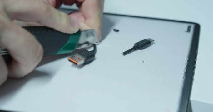 Person cutting open a USB cable to modify it, showing electronic repair risks, damaged wires and unsafe handling.