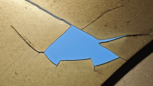Abstract view of a damaged structure with fractured surfaces, bright blue sky visible through jagged openings, showing destruction and new perspective